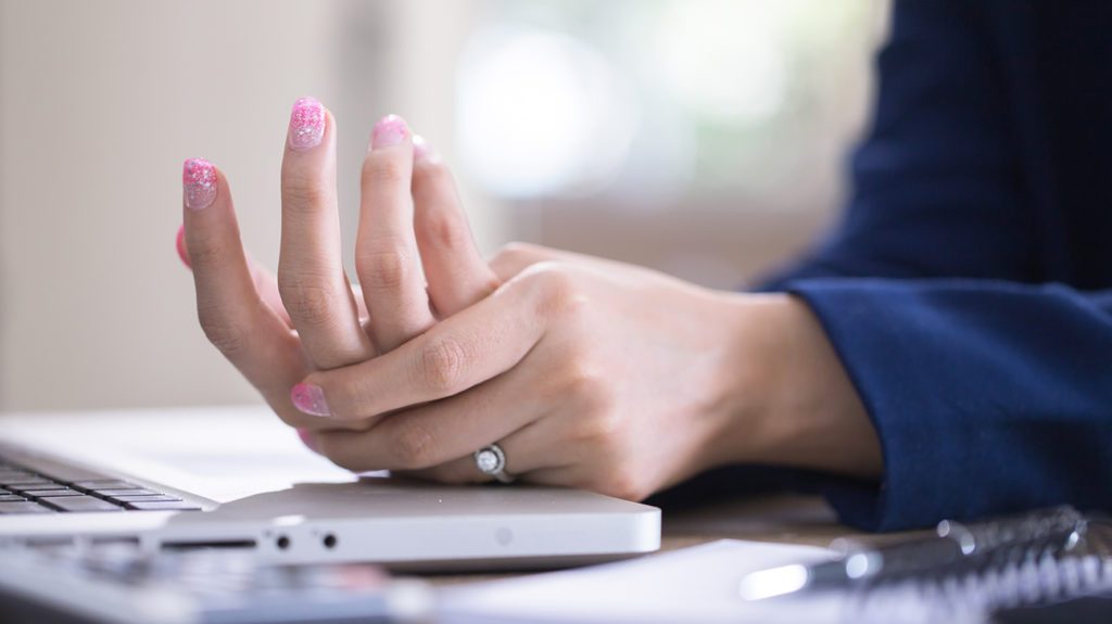 woman at a computer holding her hand in pain due to inflammation